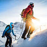 Mountain climbers leading up a snowy ridge at sunrise.