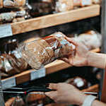 Young Asian woman carrying a shopping basket grocery shopping in a supermarket, shopping for packaged fresh wholegrain bread in the bread aisle. 