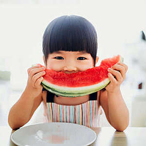 Asian little girl eating a slice of watermelon at home.